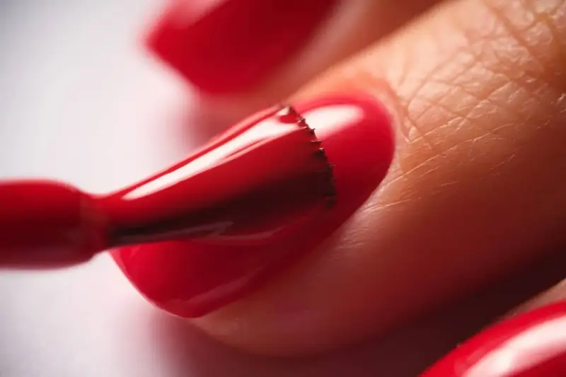 Application d'un vernis rouge vif sur un ongle. Le temps de séchage du vernis à ongles est crucial pour un fini parfait.
